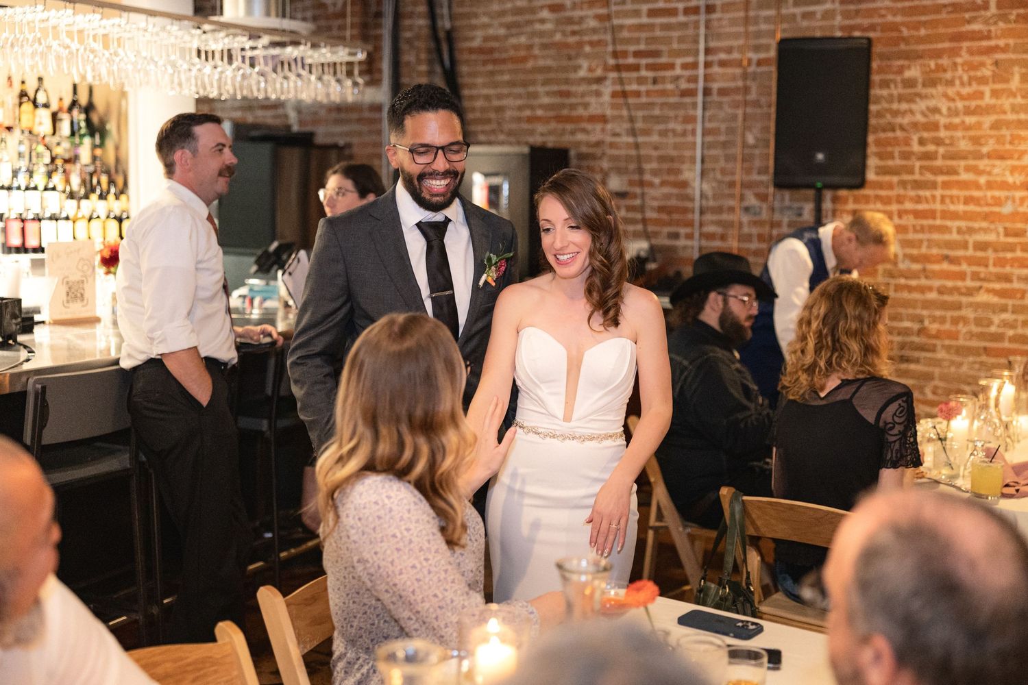 Wedding reception celebration in a rustic brick-walled venue with string lights.