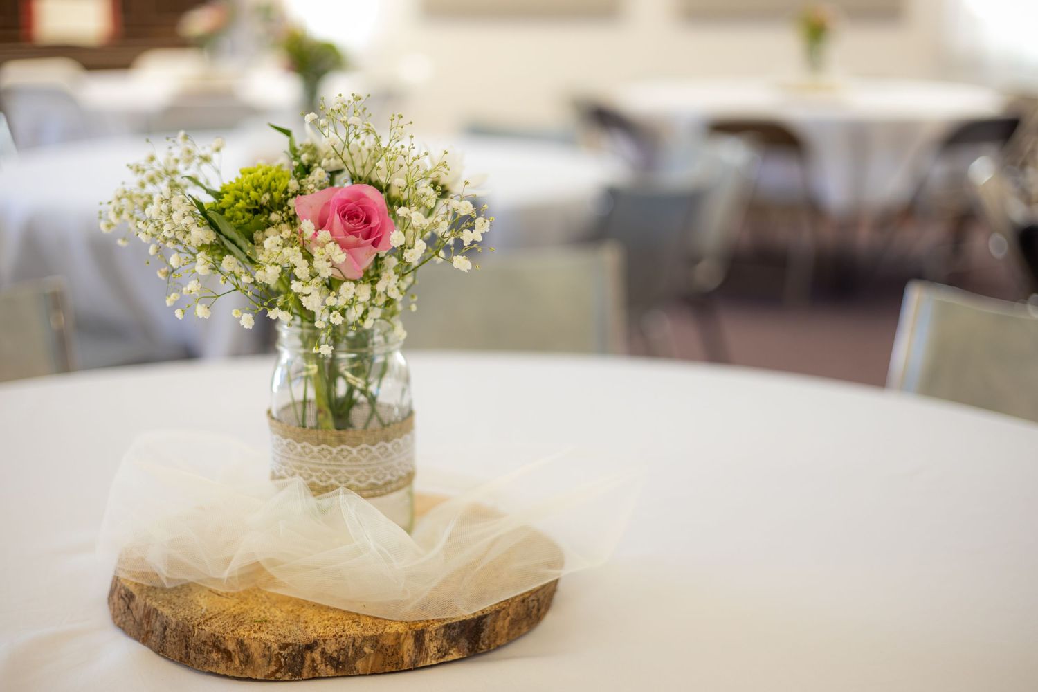 Simple floral centerpiece with roses on wooden slice at wedding reception table.