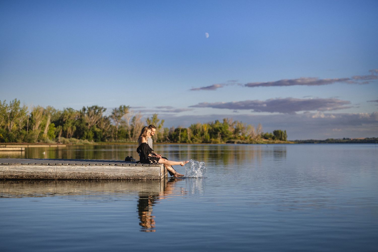 Person splashing water with feet while sitting on wooden dock at sunset.