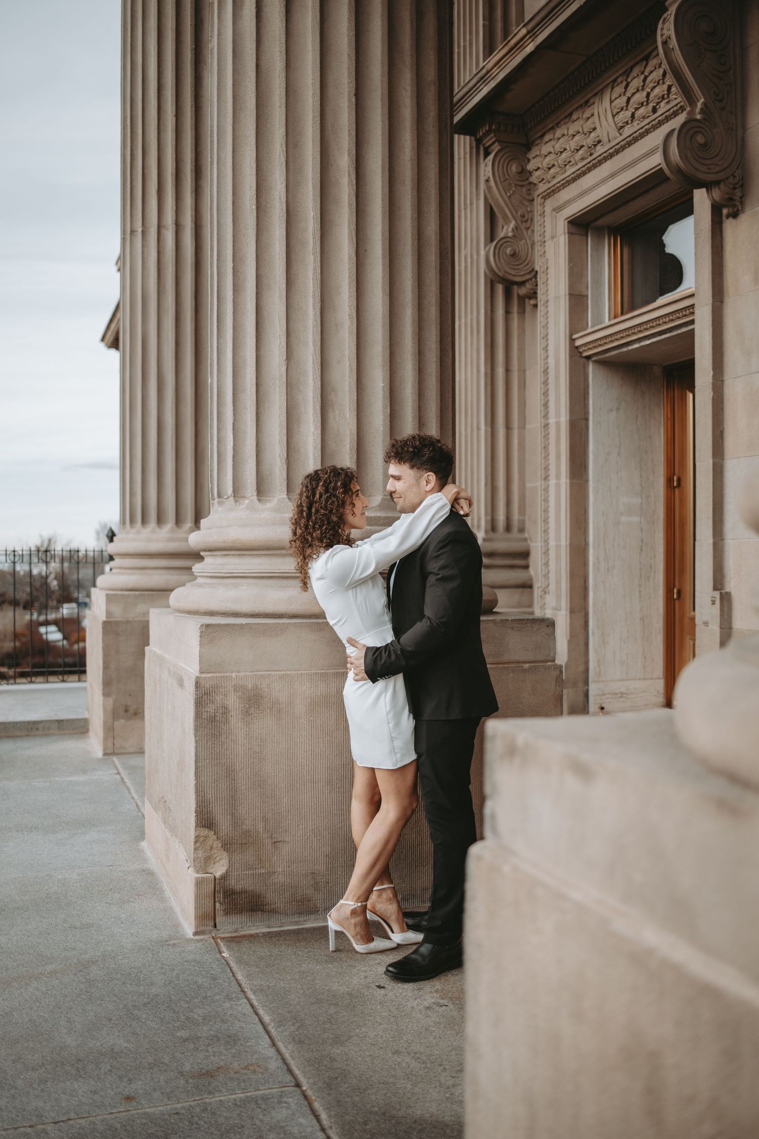 A couple embraces against classic stone columns on an elegant building exterior.