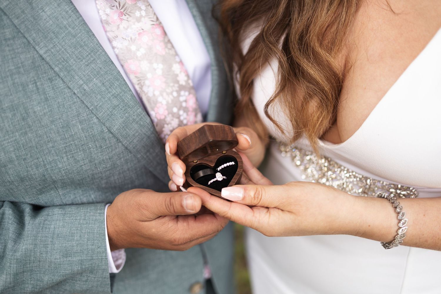 Close up of hands exchanging wedding rings during outdoor ceremony.