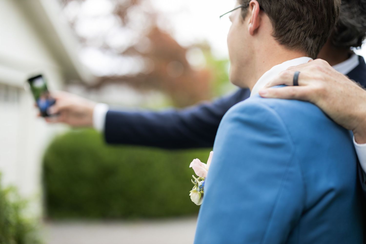 A person wearing a blue suit jacket holds a phone during what appears to be a wedding ceremony.