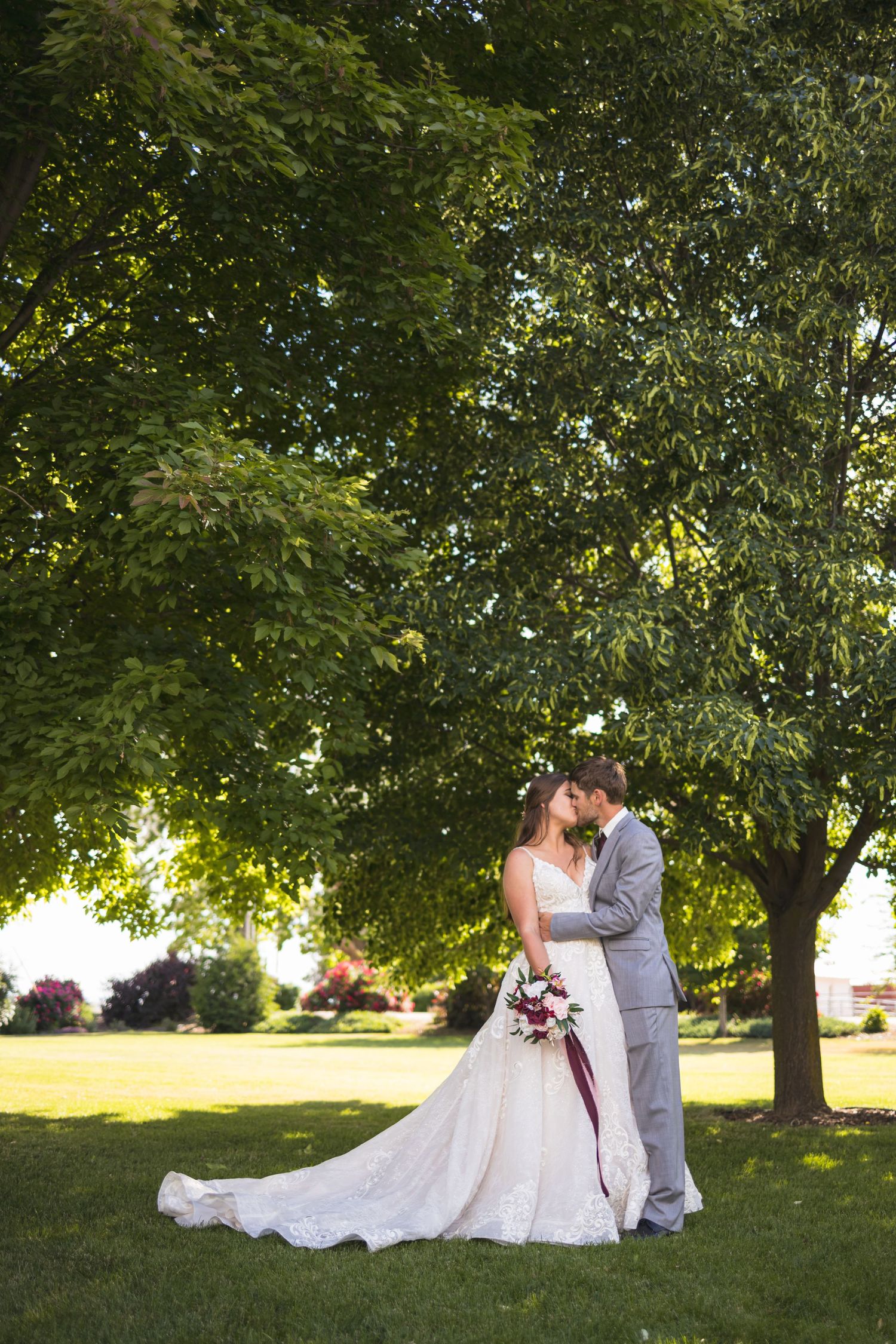 A couple shares a romantic moment under trees during their outdoor wedding ceremony.
