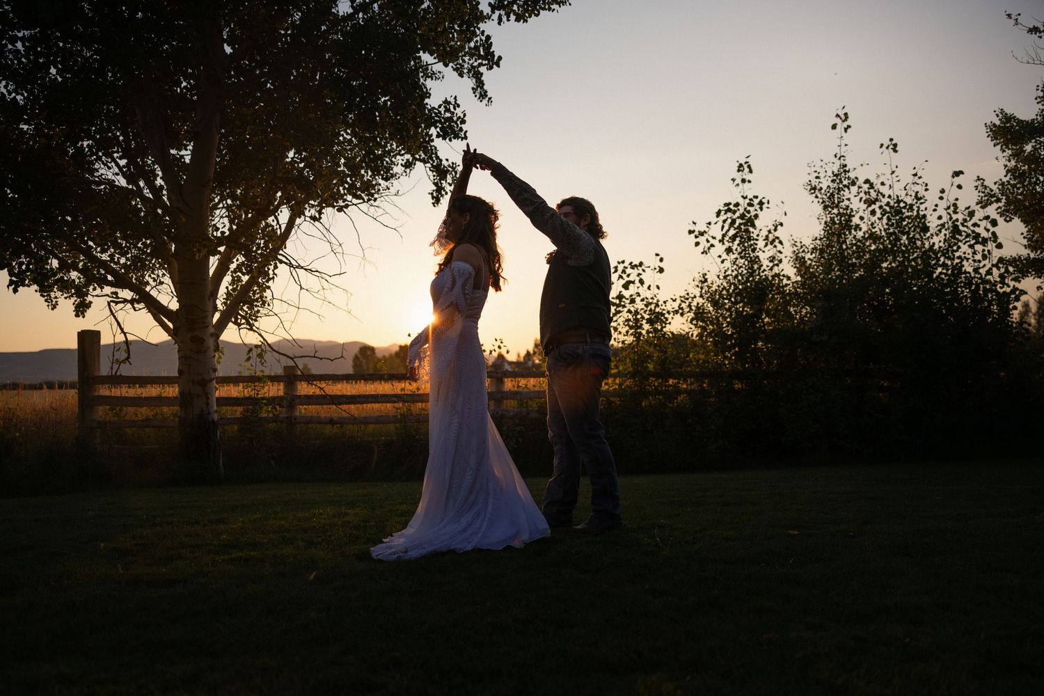 Silhouettes of a dancing couple at sunset with trees and a field in the background.