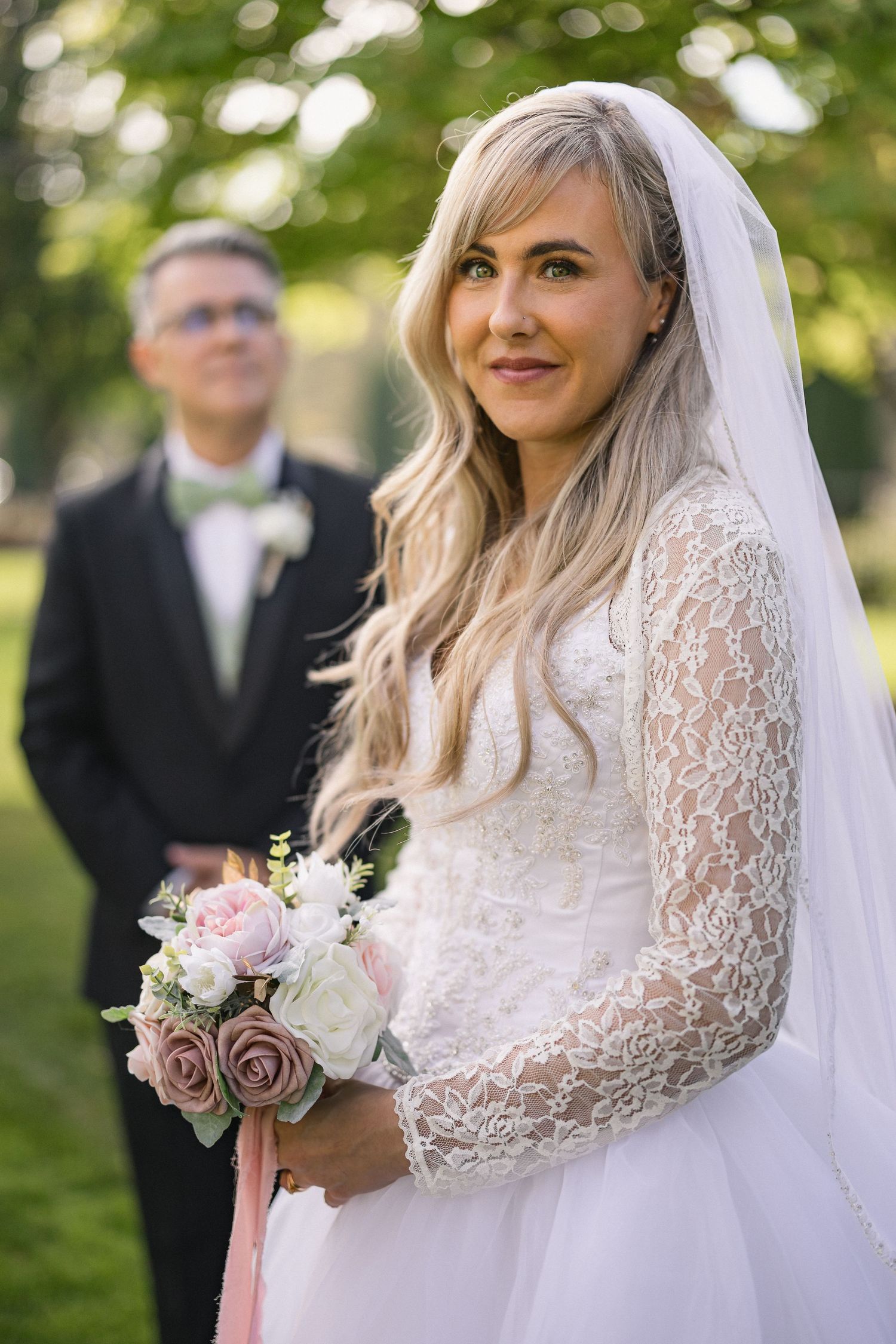 Elegant outdoor wedding portrait with bride in lace dress and flowing veil.