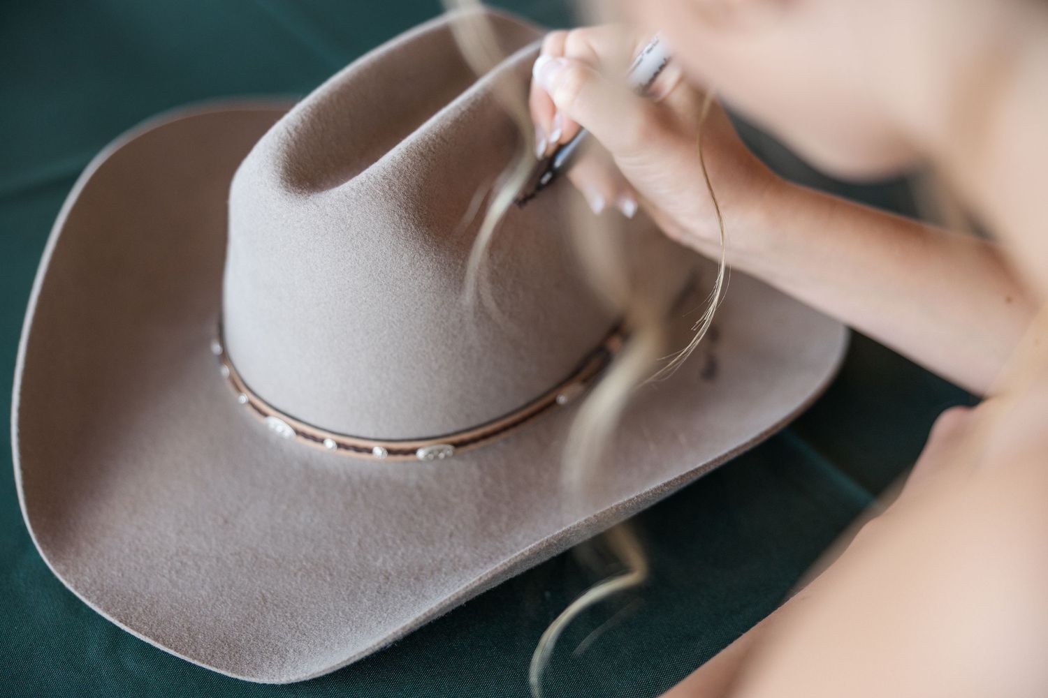 A beige cowboy hat with decorative studded band rests against a dark green background.