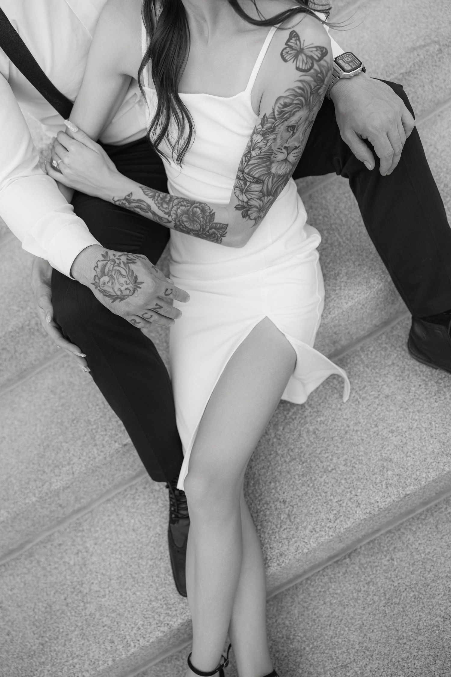 Black and white photo showing tattooed arms and legs on concrete steps.