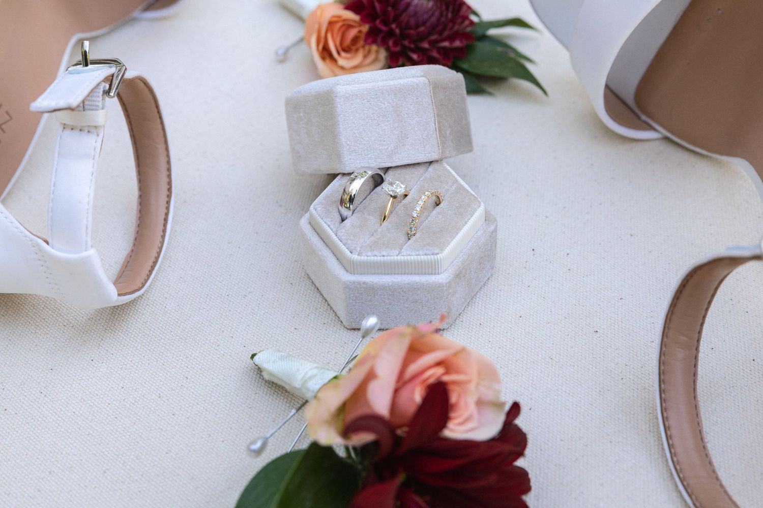 Wedding rings in a hexagonal box surrounded by floral boutonnières and white heels.