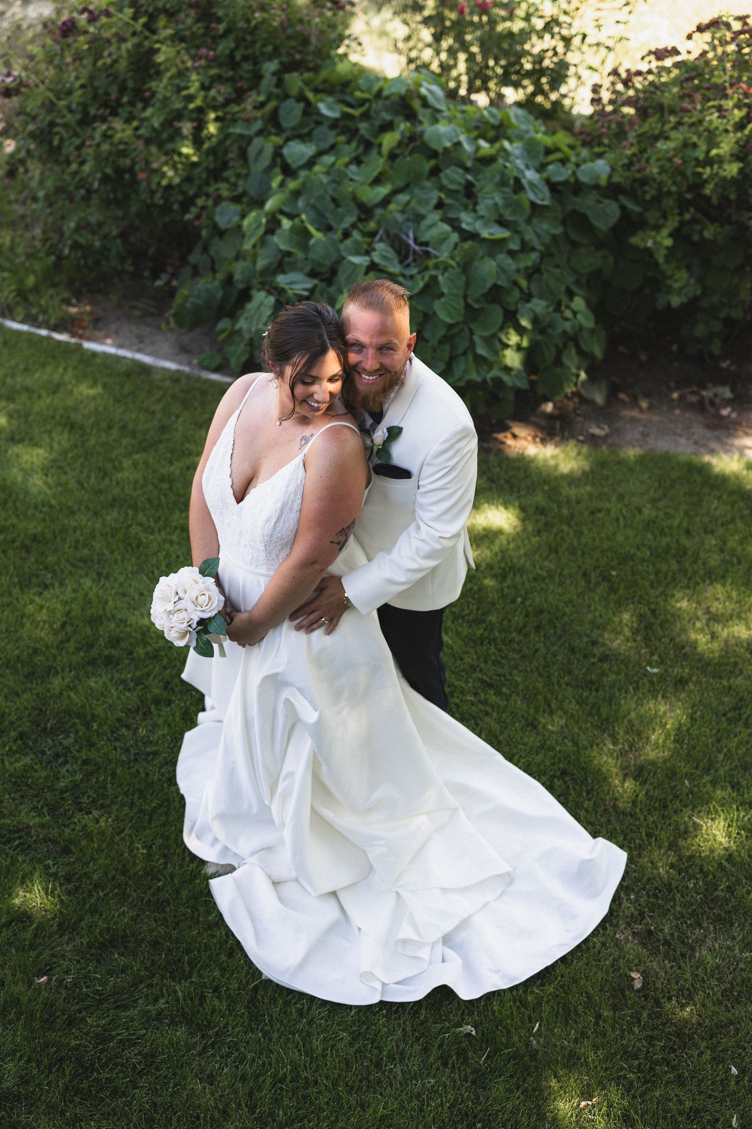 Romantic wedding portrait of a couple embracing on grass with flowing white dress.