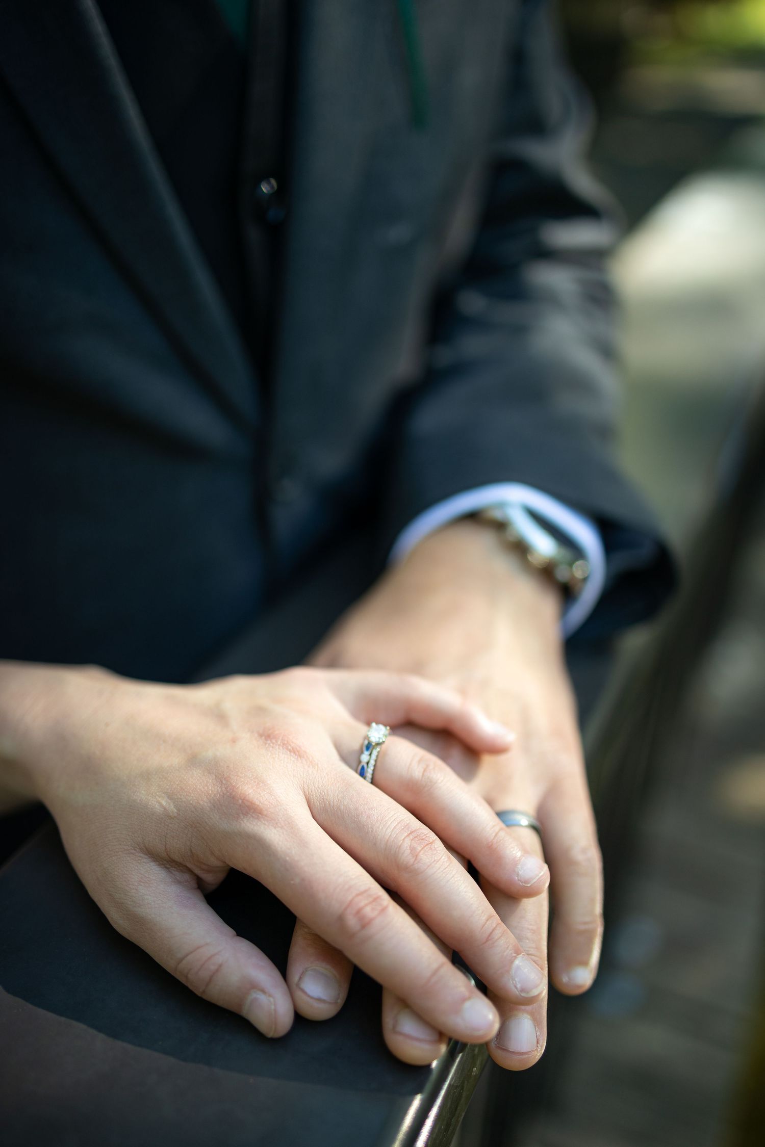 Close-up shot of wedding rings and hands against a dark background.