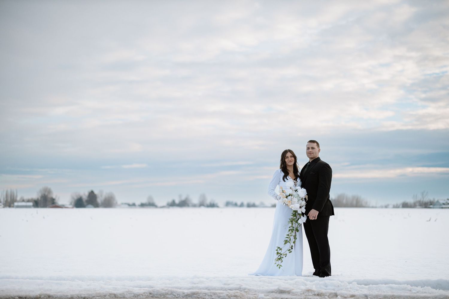 Winter wedding portrait with dramatic sky and snow-covered field in background.