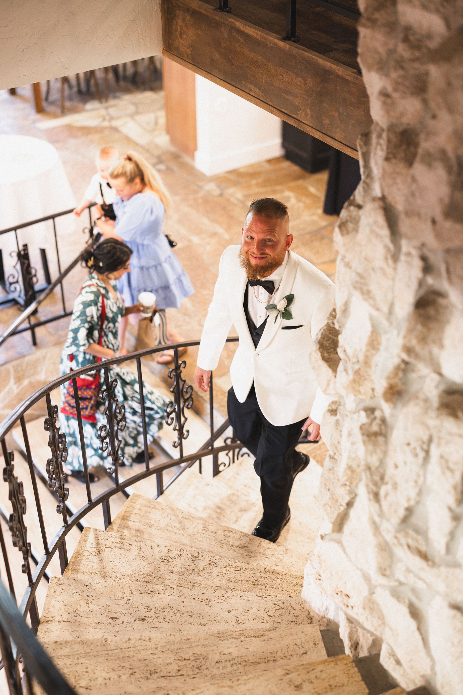Person in white tuxedo jacket ascending stone staircase during wedding celebration.