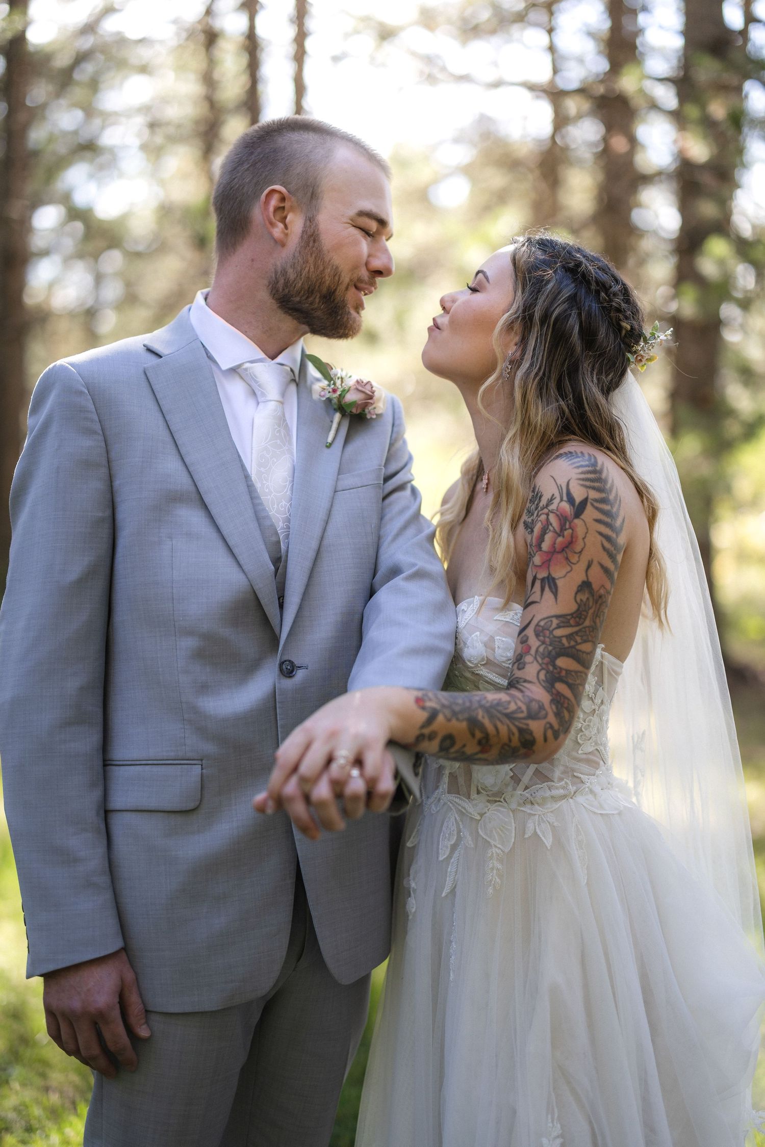 A romantic wedding portrait of a couple in a forest setting with sunlit trees in the background.