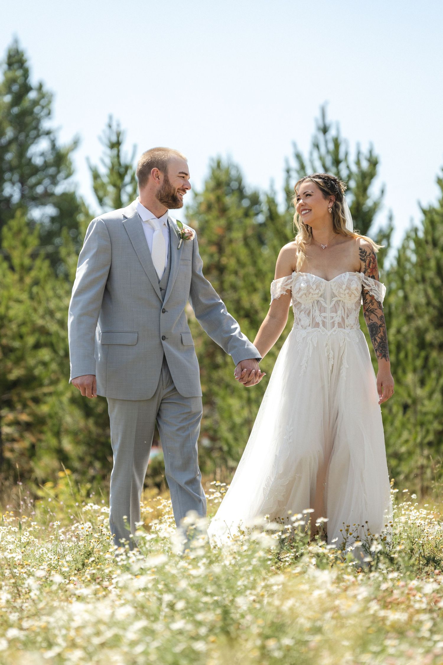 Newlyweds share a tender moment while walking through a meadow of white flowers on their wedding day.