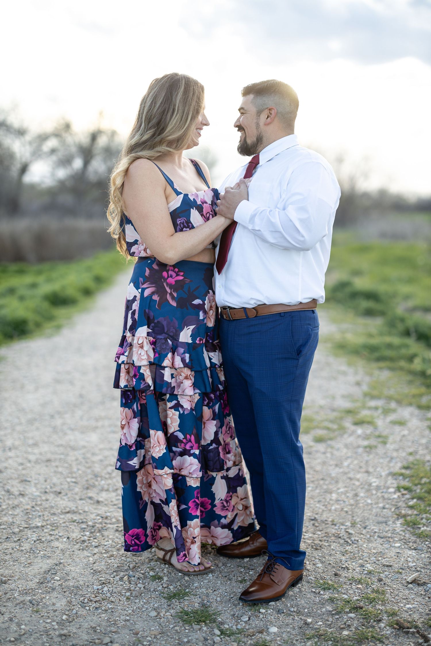 Dancing couple in floral dress and formal wear on gravel path at sunset.