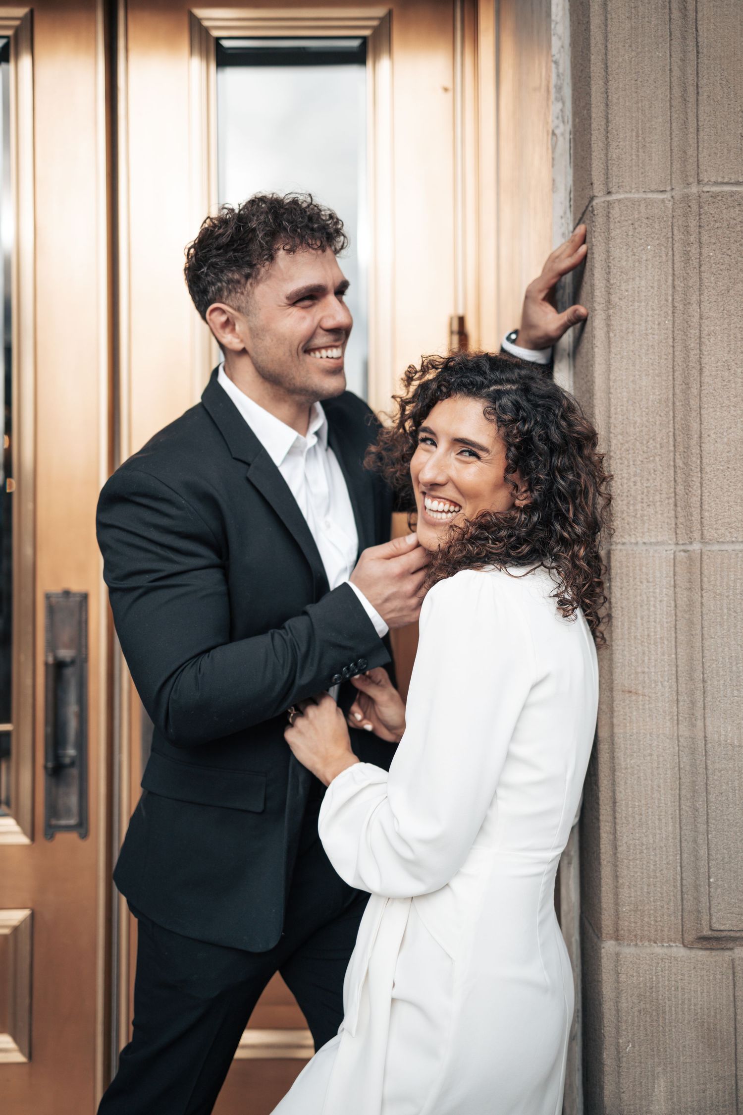 A joyful couple in contrasting black and white outfits share an intimate moment by an elegant doorway.