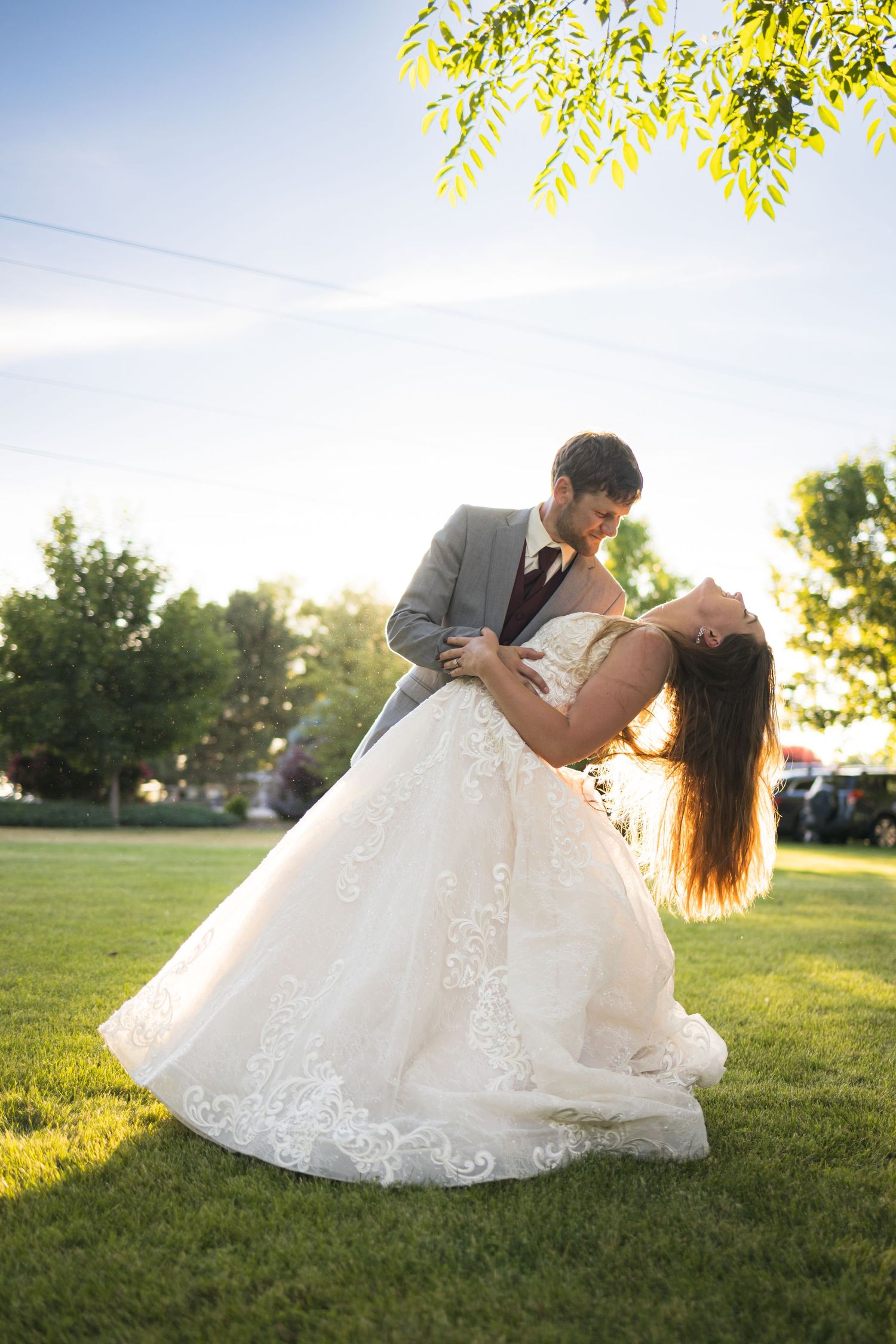 A romantic dip pose on a grassy lawn during wedding photos at sunset.