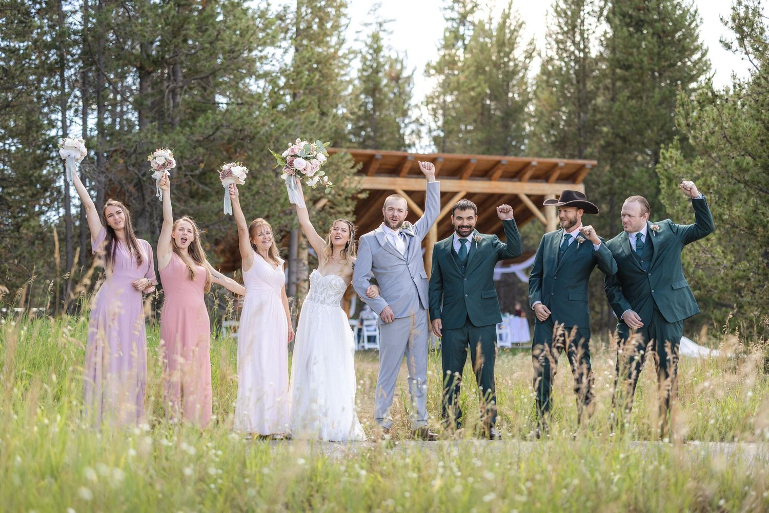 Wedding party celebrating outdoors with groomsmen in dark suits and bridesmaids in light dresses.