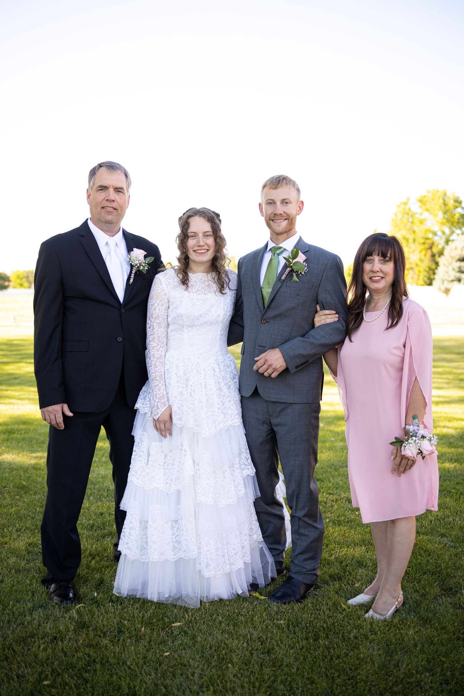 Small wedding group poses outdoors wearing formal attire including white gown and pink dress.