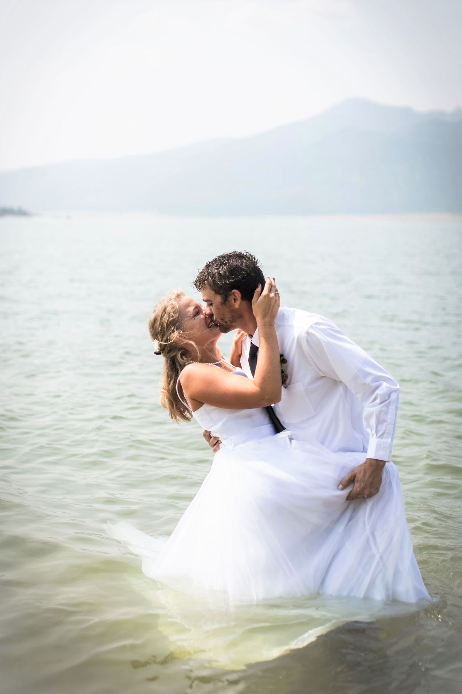 Romantic portrait of newlyweds kissing in the water with bride's dress floating.