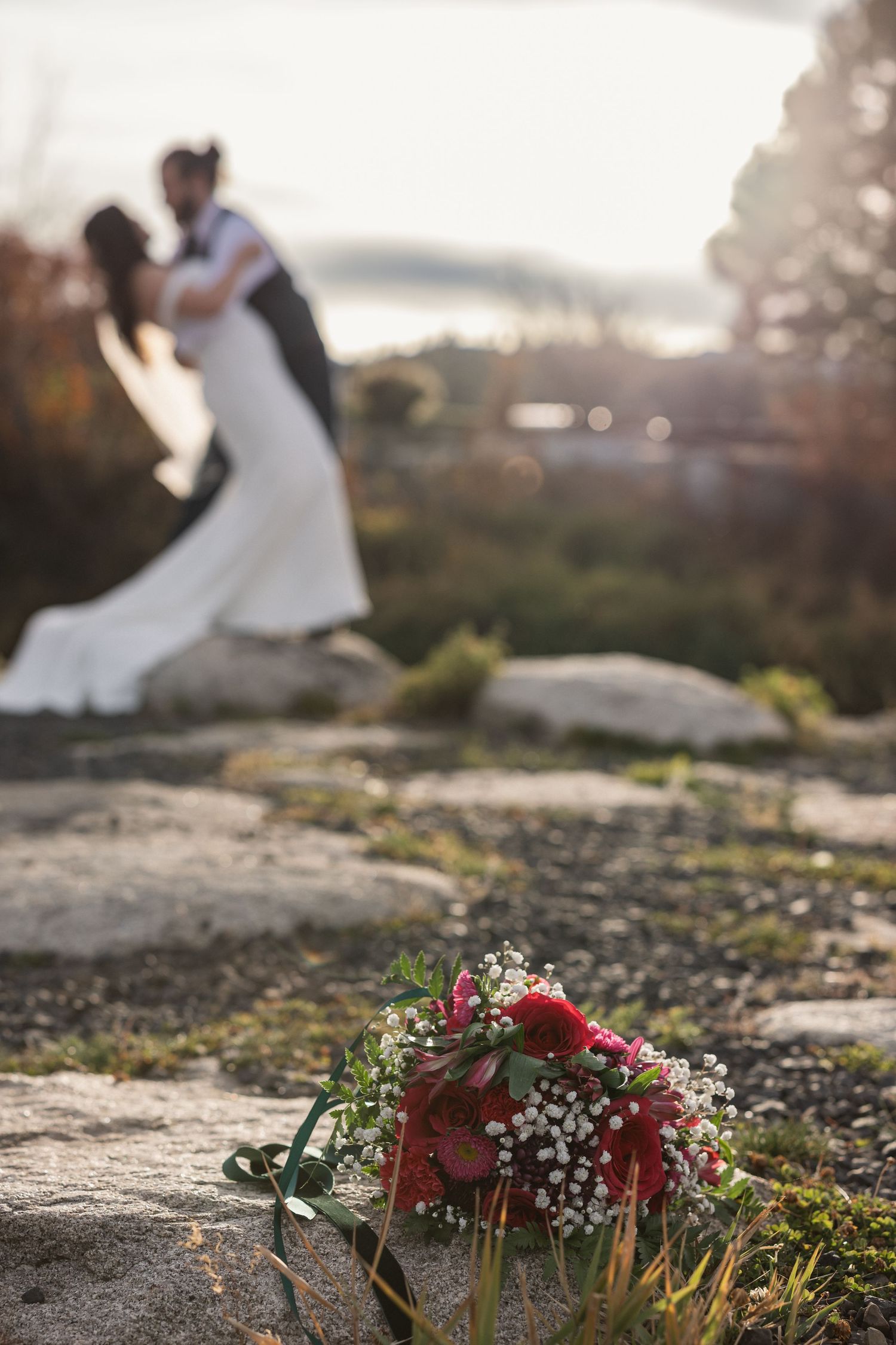 Red and white bridal bouquet in foreground with blurred couple in background.