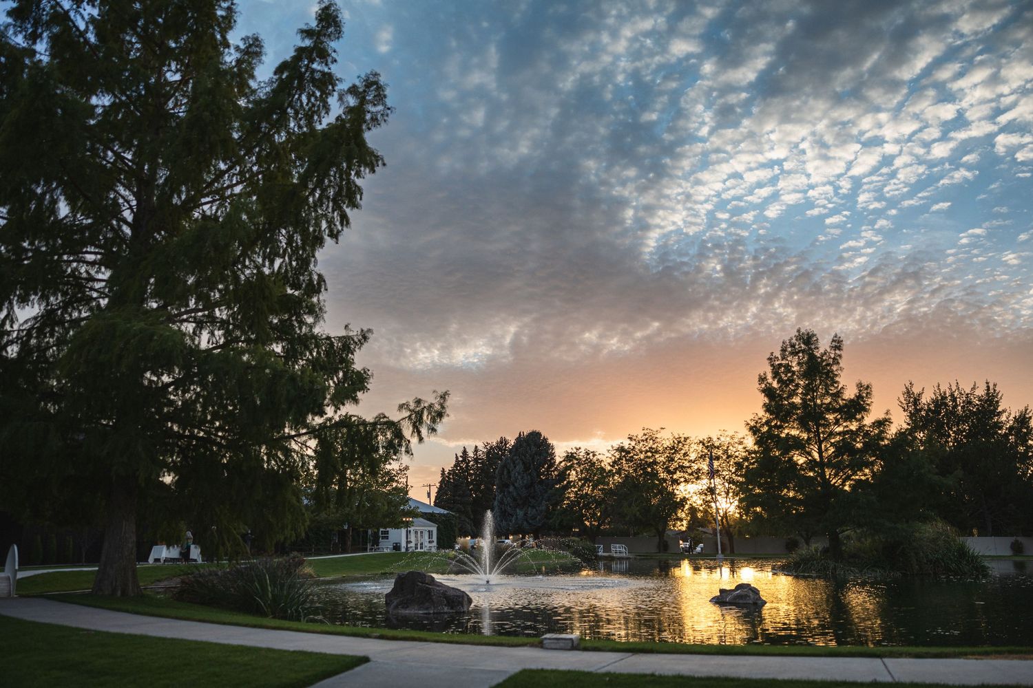 Sunset view of a white chapel and fountain with dramatic clouds reflecting on peaceful water.