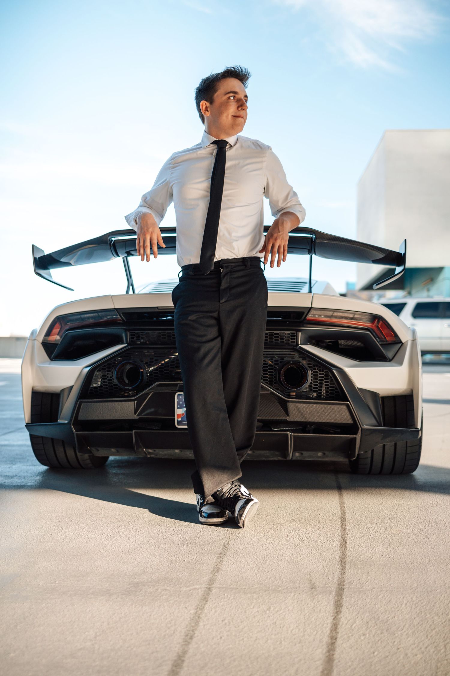 Person leaning against rear wing of white Lamborghini with doors up in parking structure.