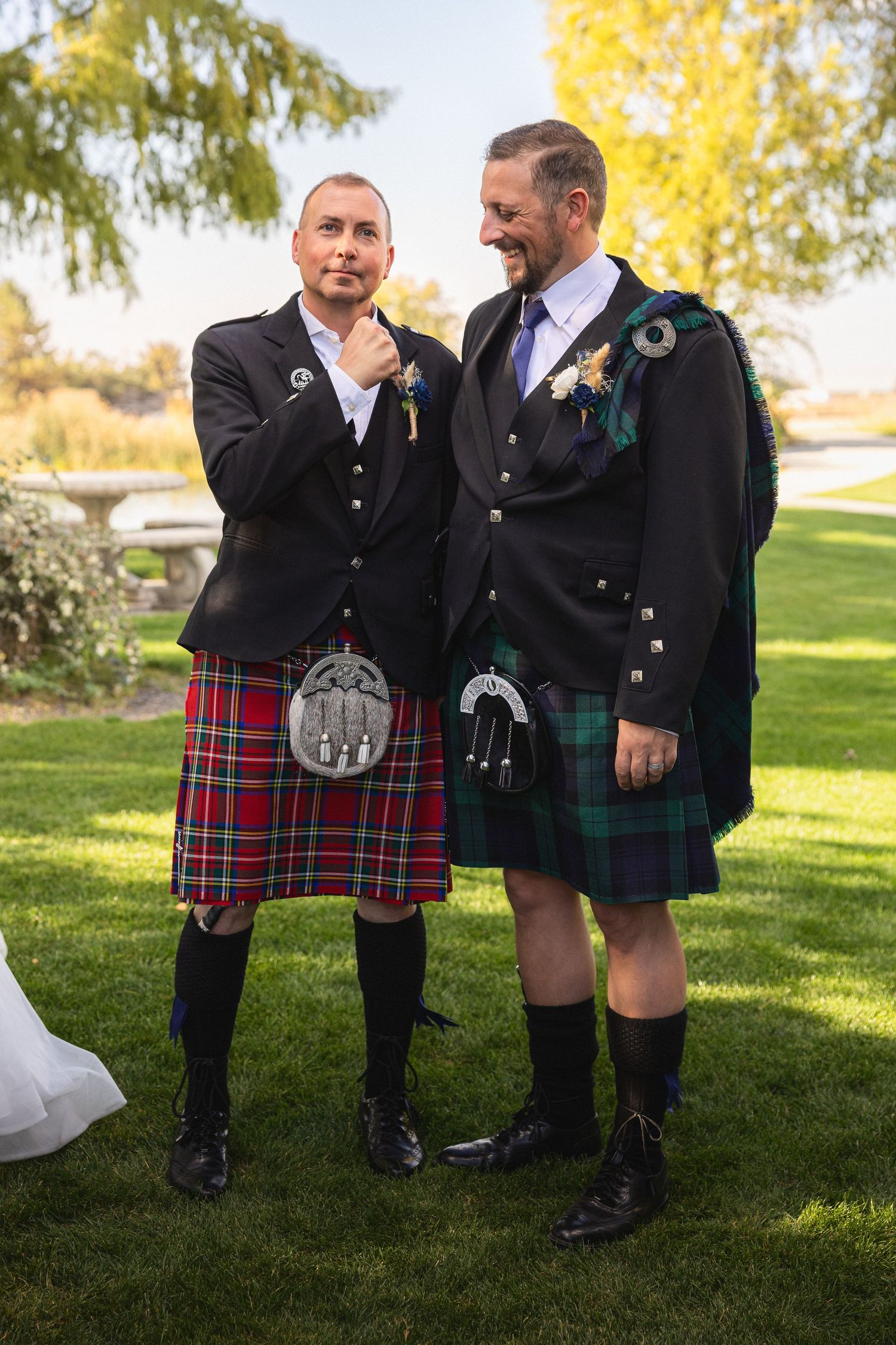 Two people in traditional Scottish kilts and formal jackets share a moment on the lawn.