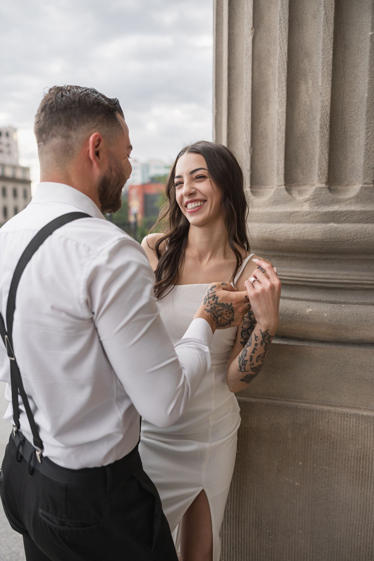 A couple in formal attire share intimate moments while posing against classic stone columns.
