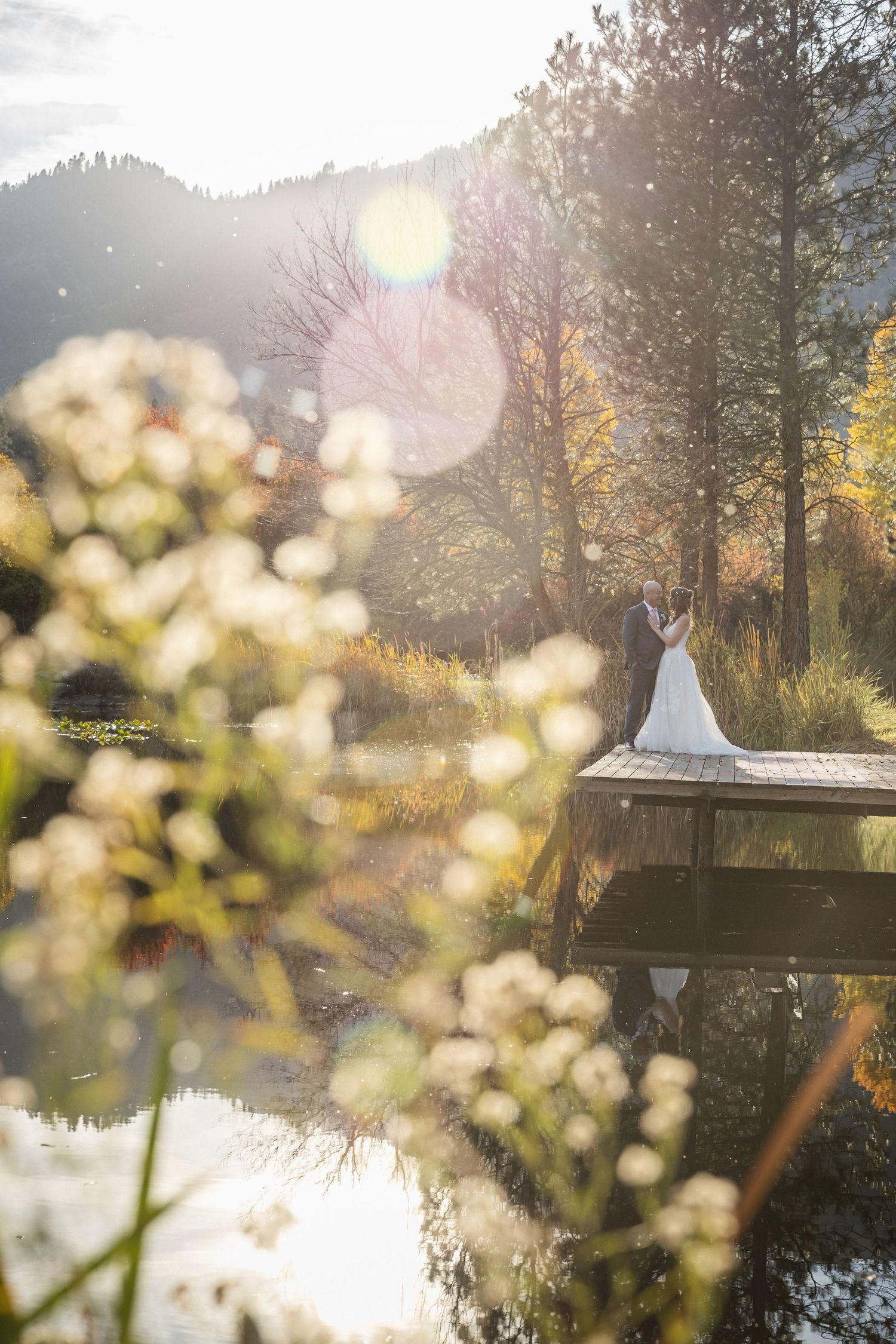 Dreamy wedding photo on a dock with lens flare and autumn reflections in the water.