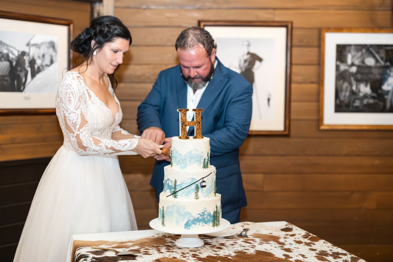 Newlyweds cut into their mountain-themed wedding cake in a wood-paneled room.