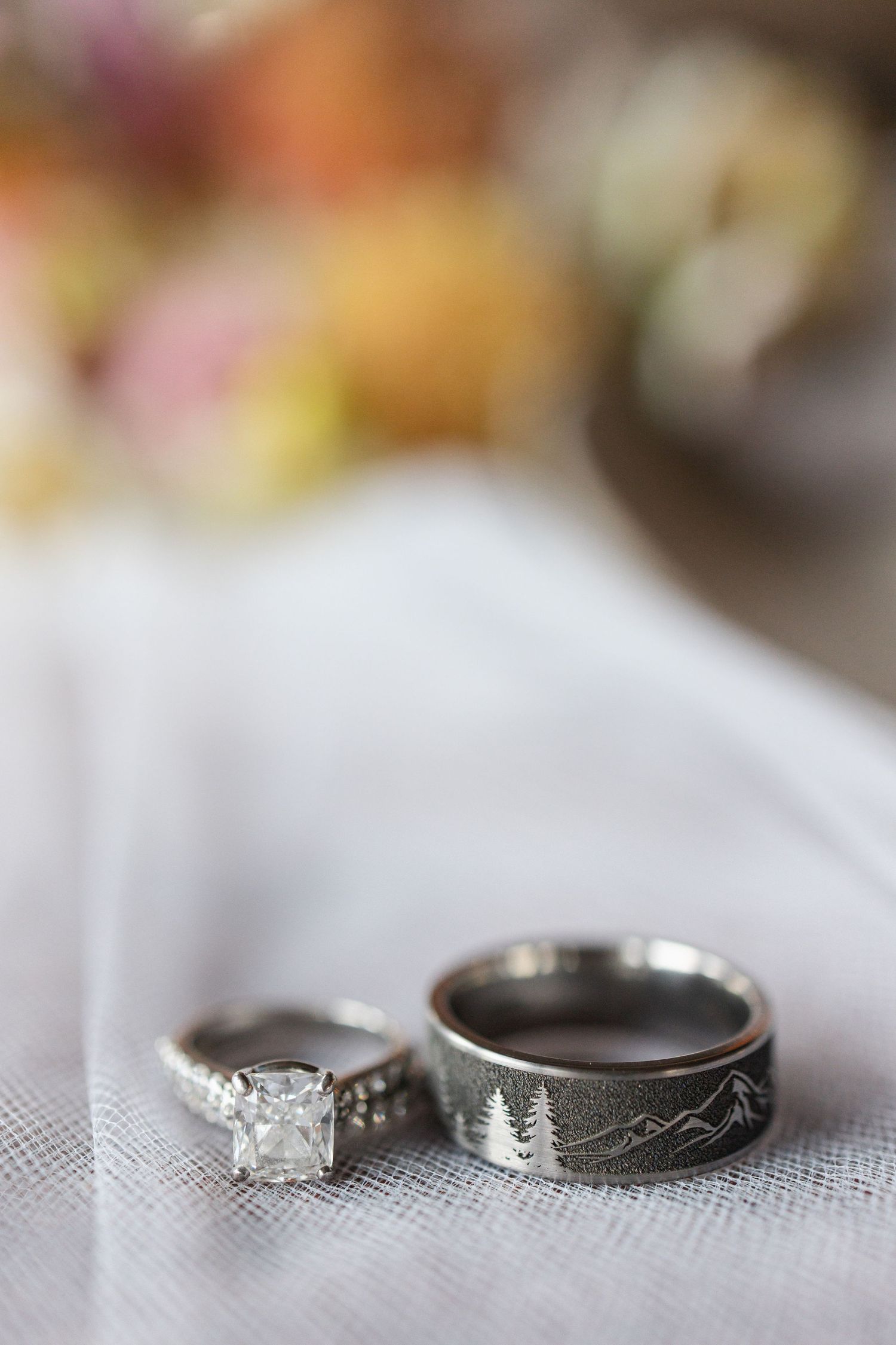 Wedding rings with mountain and forest engravings displayed on white tulle fabric.