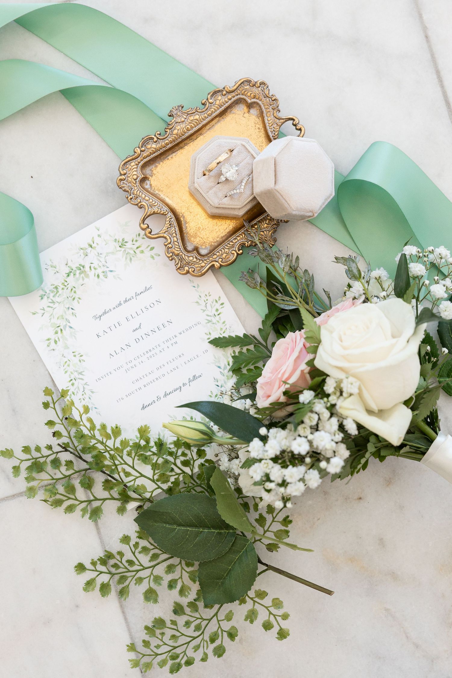 Wedding invitation with mint green ribbon, white roses, and delicate greenery arranged on vintage gold frame.