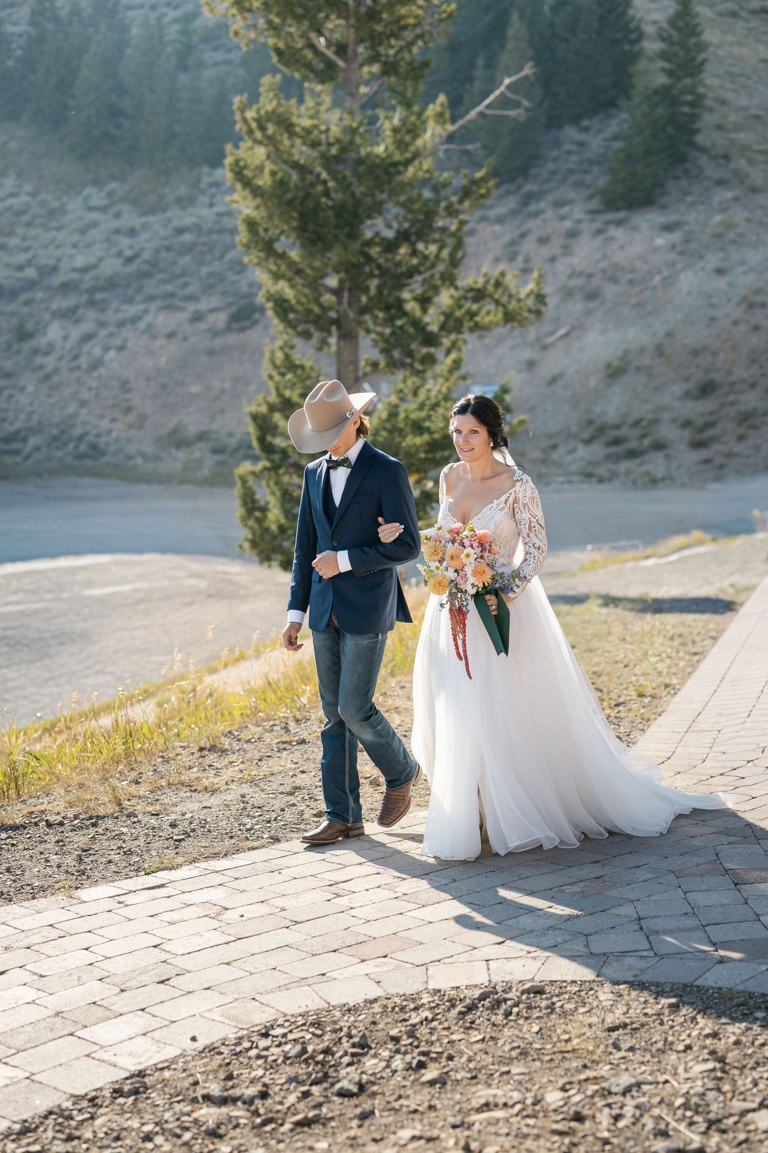 A couple walking along a stone pathway on a scenic mountainside during their wedding day.