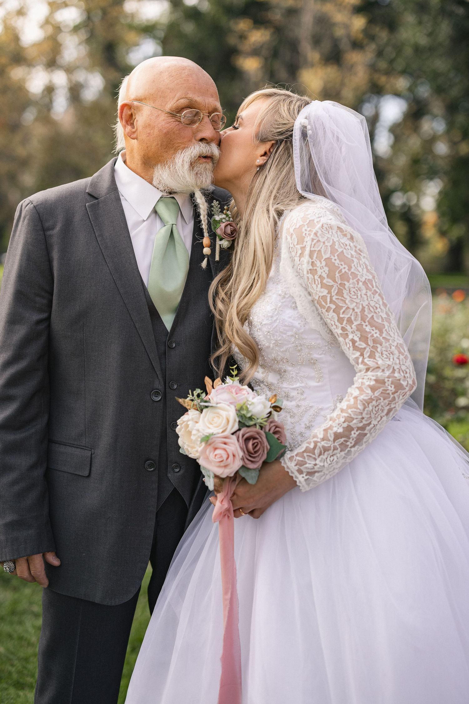 A tender moment shared between a bride and older gentleman during wedding photos in a garden setting.