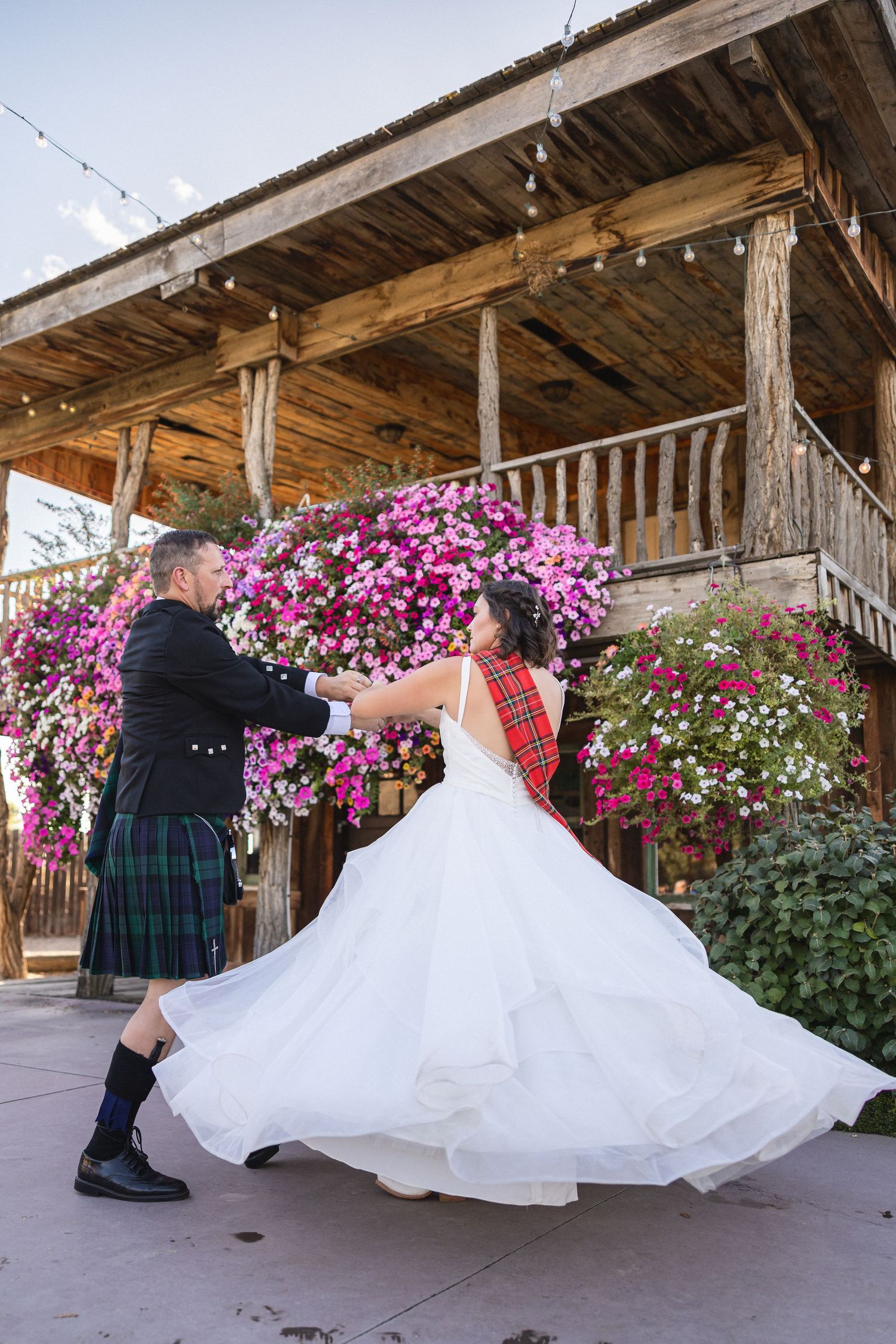 Newlyweds performing elegant dance twirl under wooden porch decorated with vibrant flowers.