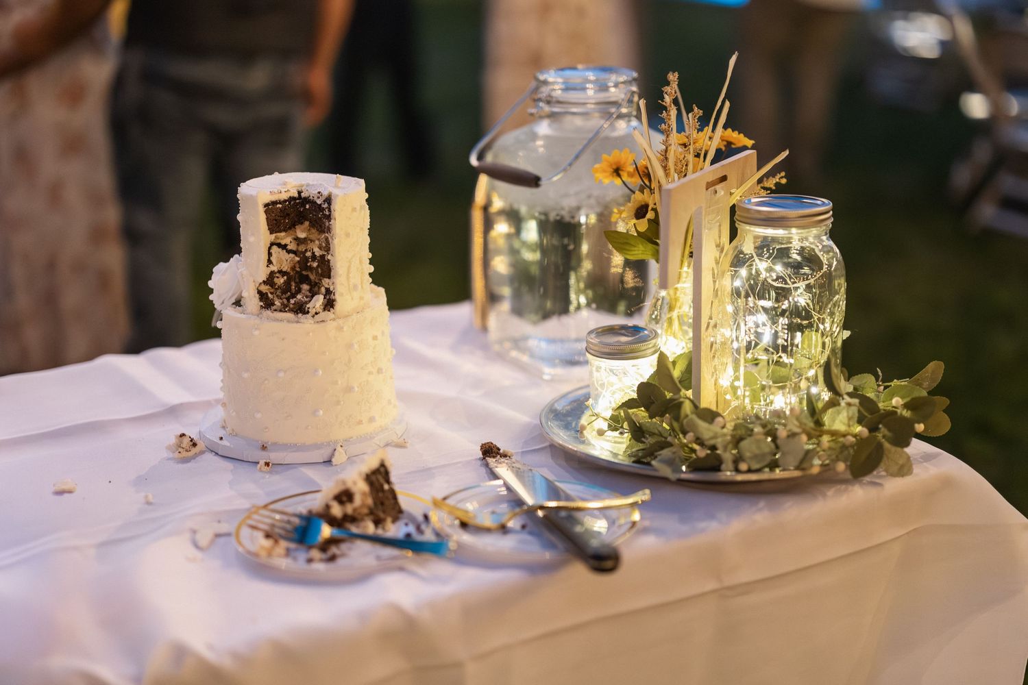 Wedding reception table with white tablecloth and decorative mason jars lit by soft lighting.