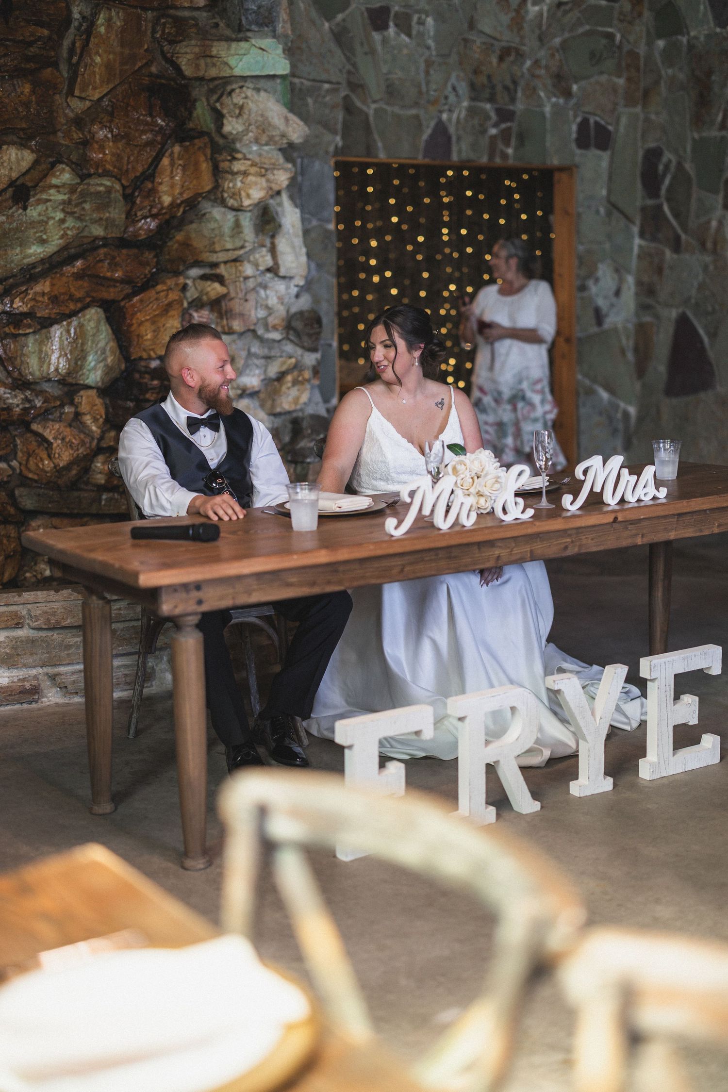 Wedding reception scene with rustic wooden table, Mr & Mrs signage, and twinkle lights in background.