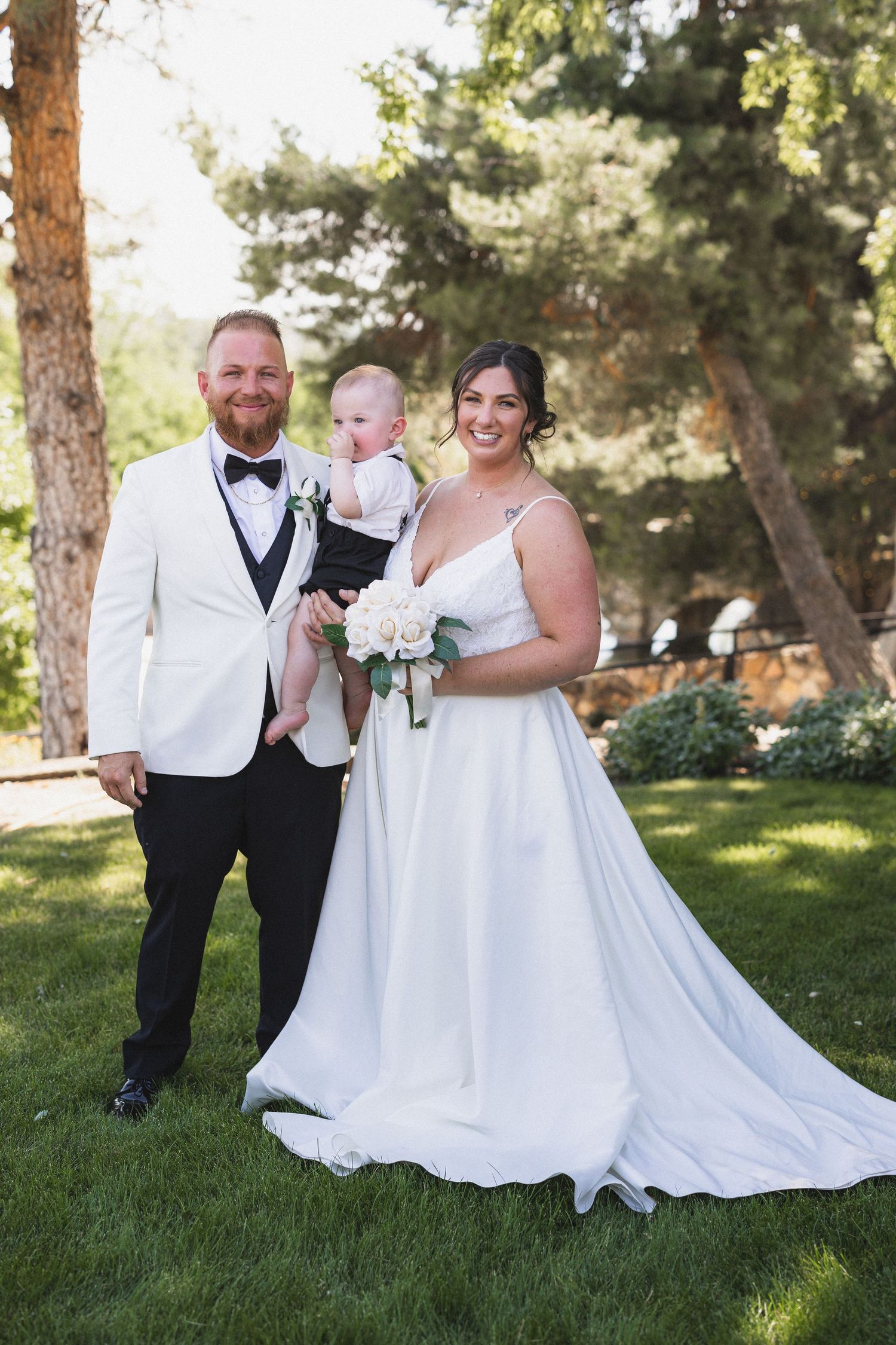 Elegant outdoor wedding photo with a couple and small child among pine trees.