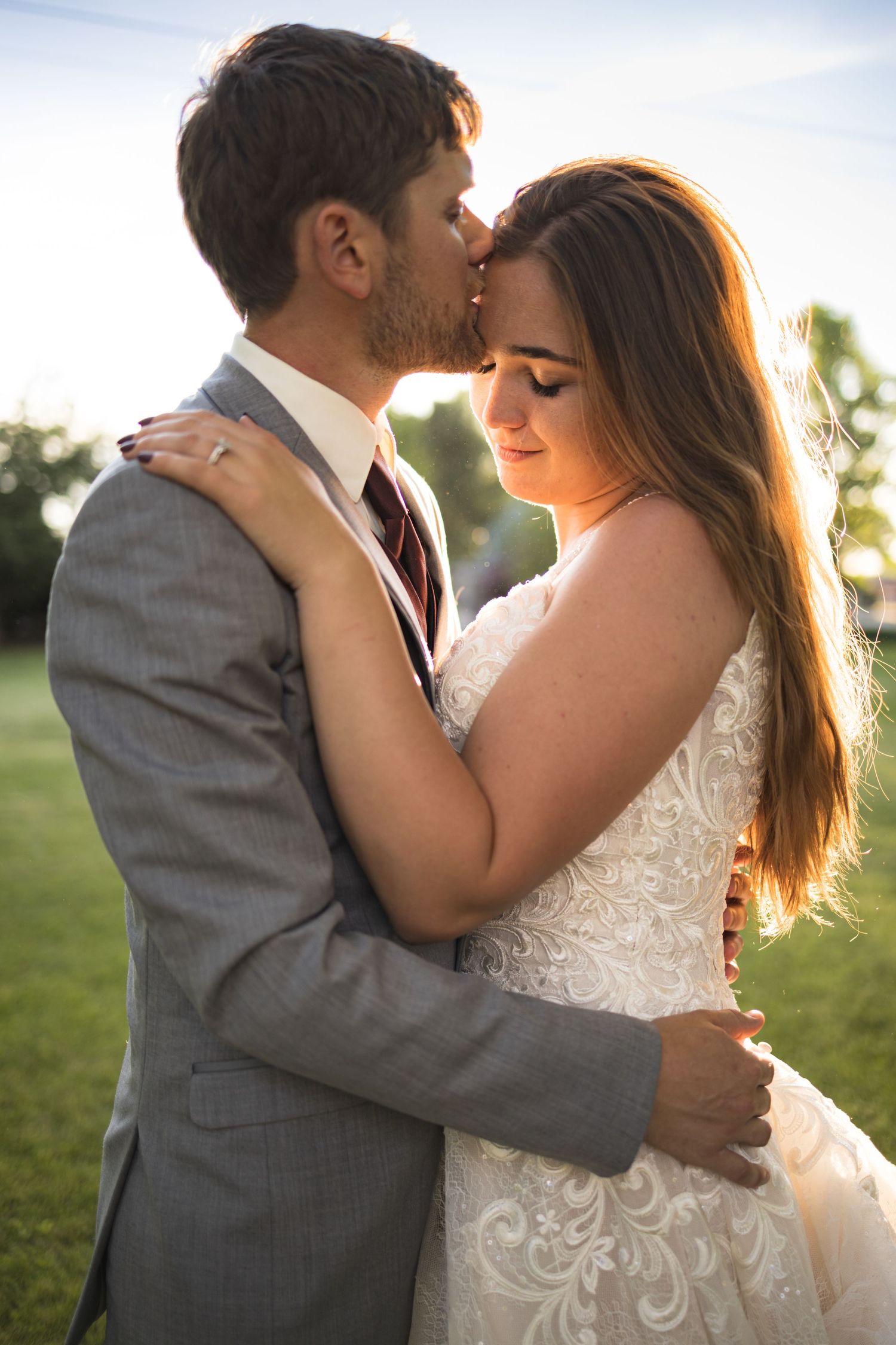 A tender embrace between newlyweds in formal attire against a sunset backdrop.