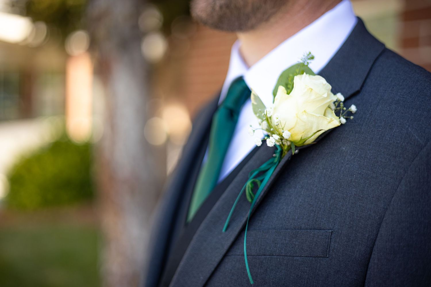Close-up of white rose boutonniere on dark suit with emerald green tie.