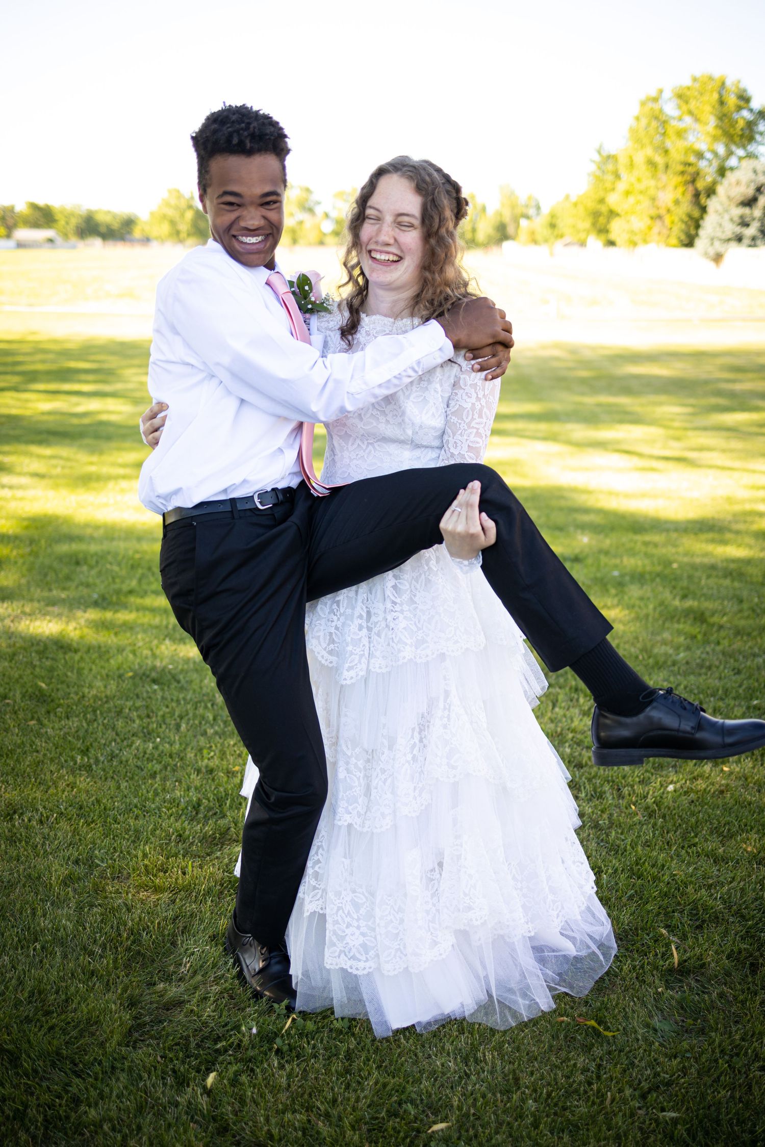 Joyful wedding couple shares playful moment with groom carrying bride outdoors.