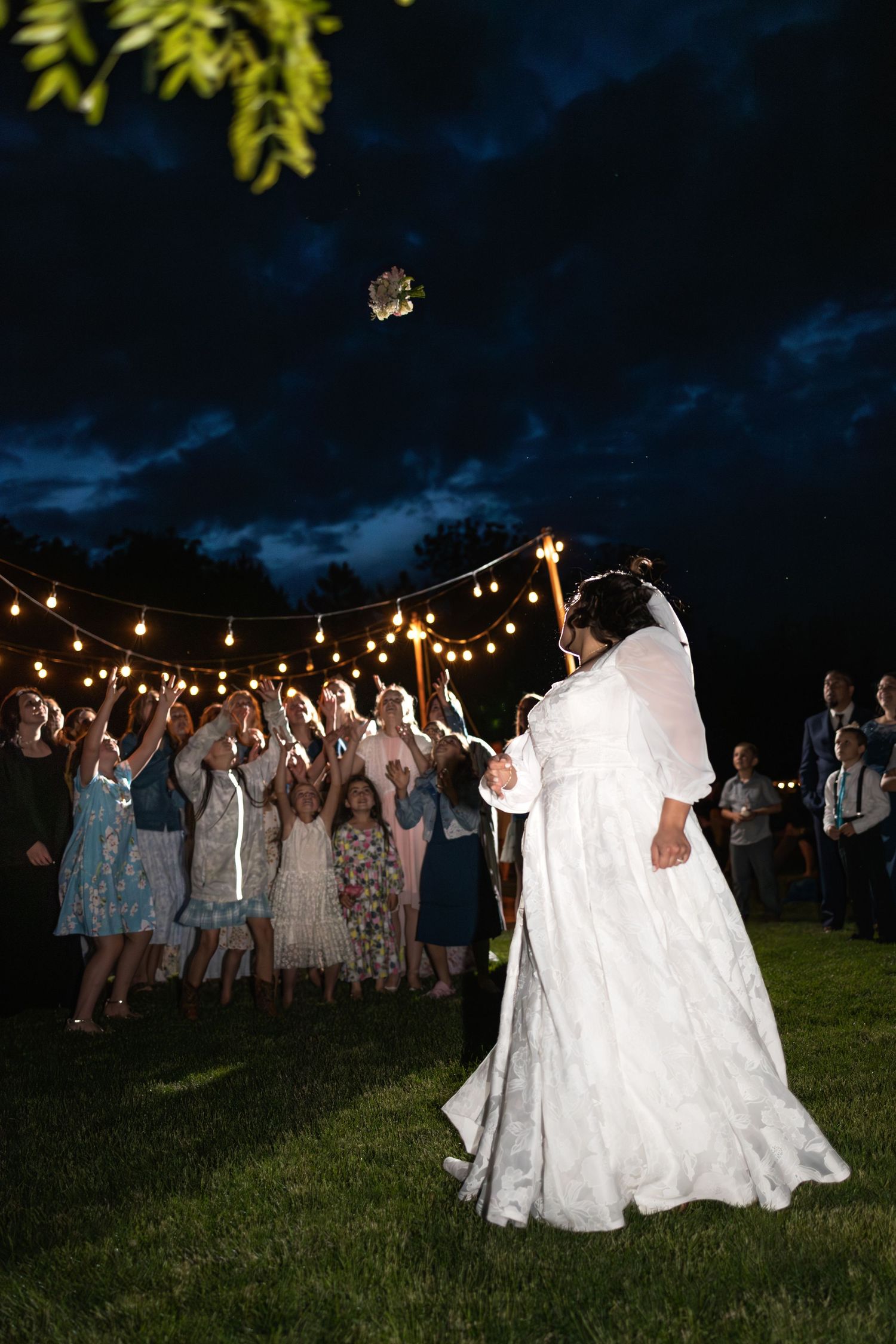 Celebration on a lawn at night with string lights illuminating dancers in white dresses.