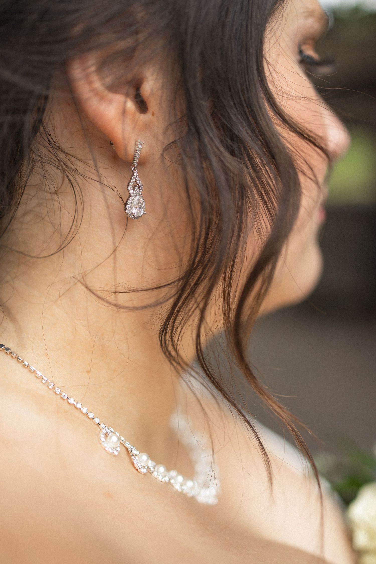Close-up of delicate crystal drop earrings and necklace on bride's neck.