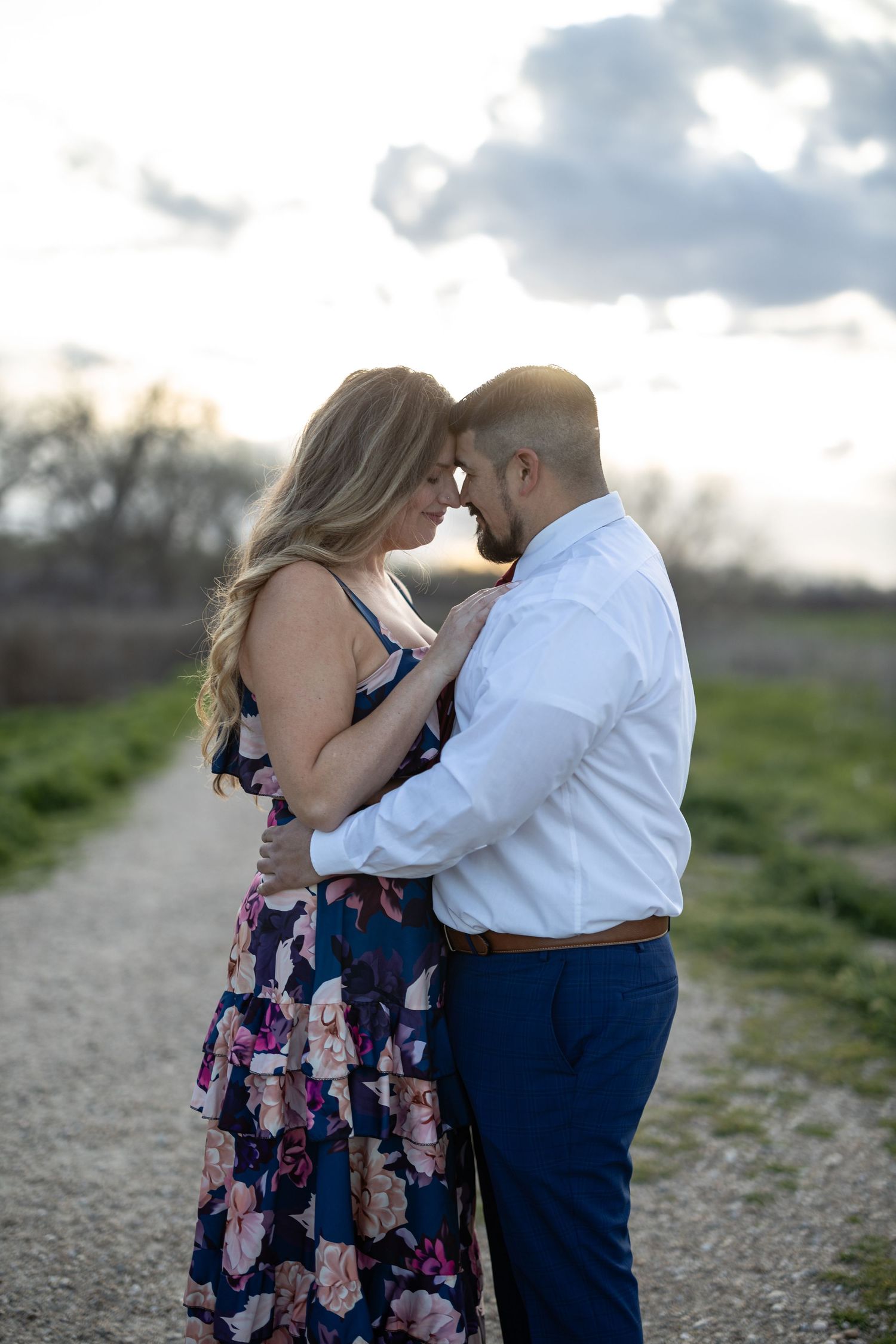 Romantic outdoor photoshoot on gravel path with sunset sky backdrop.