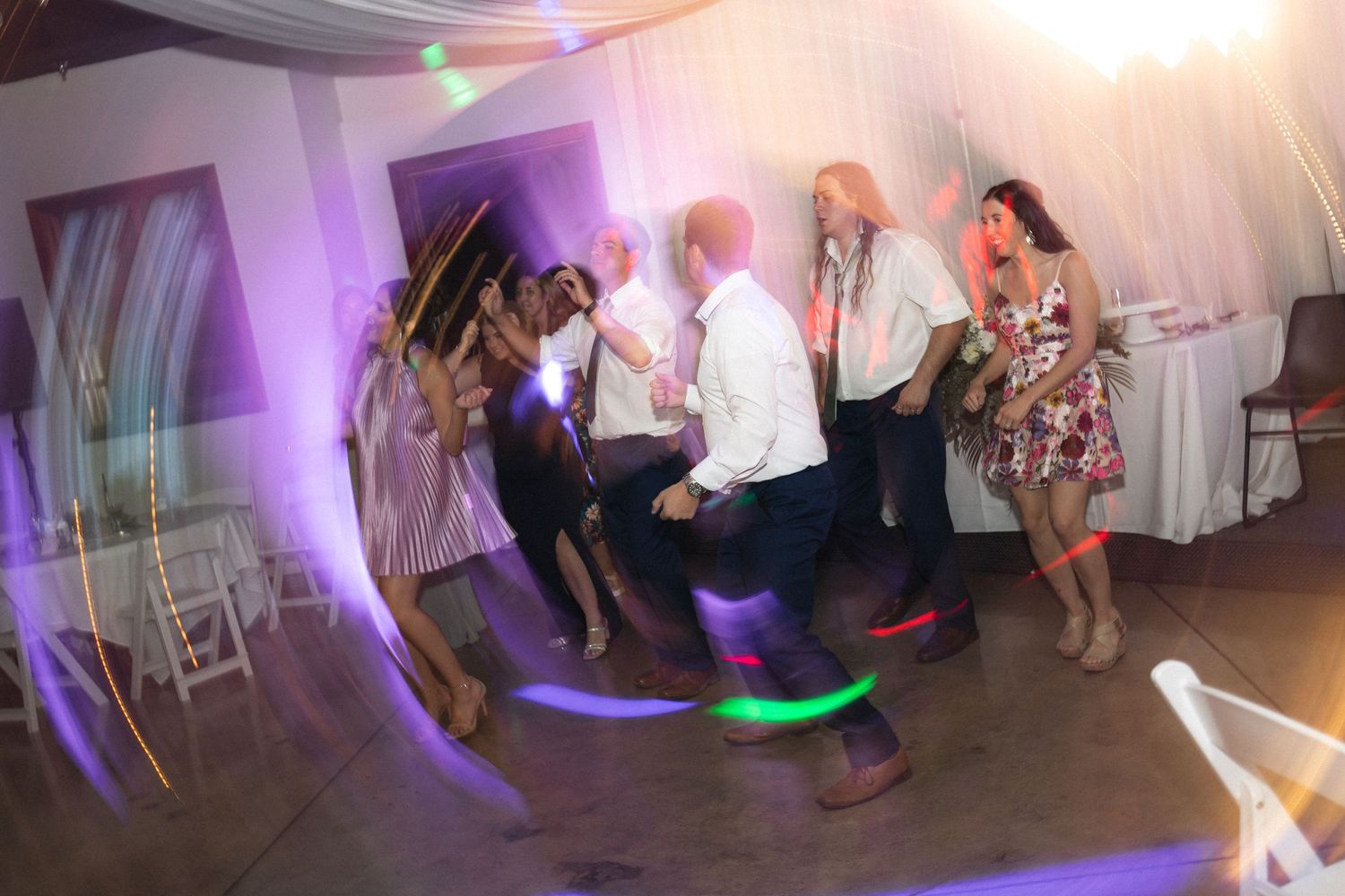 Wedding reception dance party with colorful purple lighting and guests dancing.