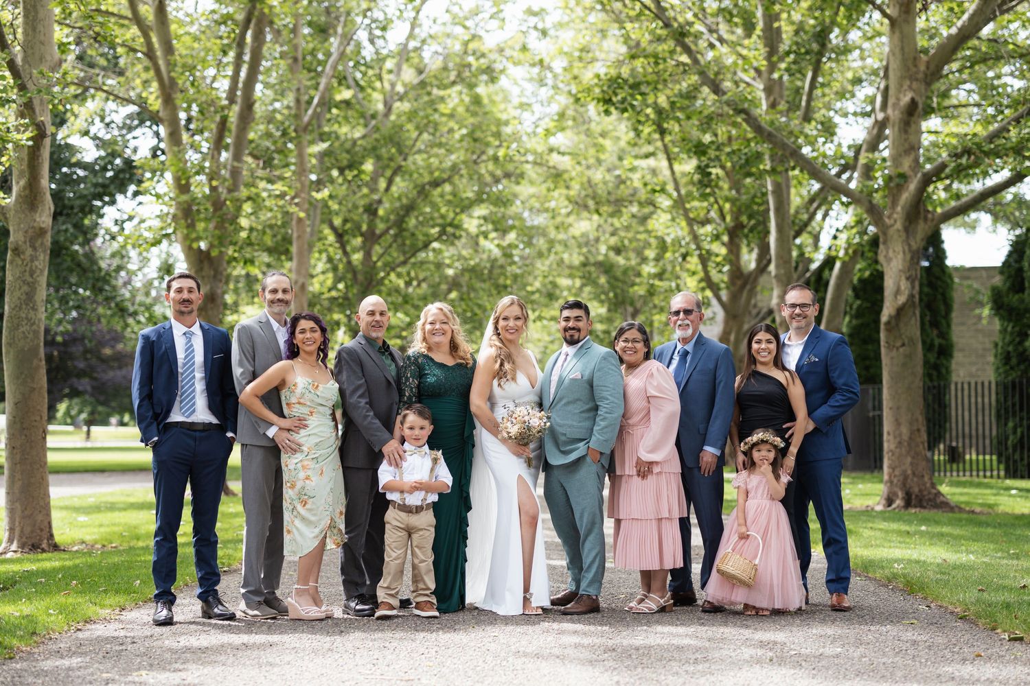Wedding party poses together on tree-lined path in coordinated formal attire.