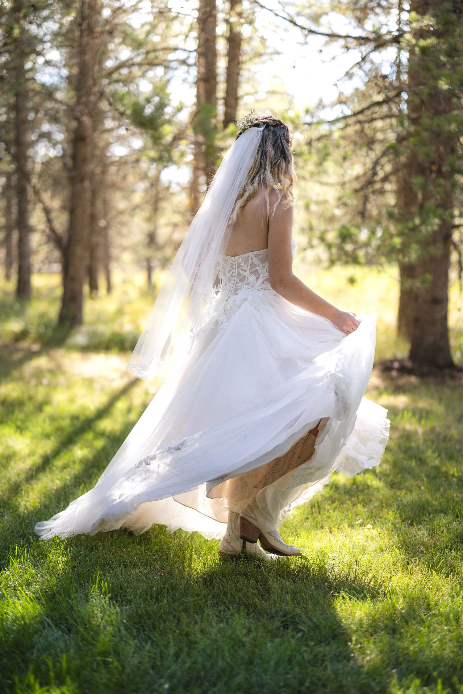 Bride in a flowing white dress twirls playfully in a sunlit forest clearing.
