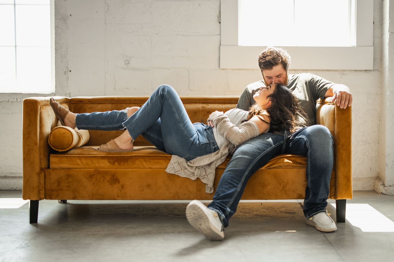 Two people relax and lounge on a wooden bench in a bright minimalist room with white walls.
