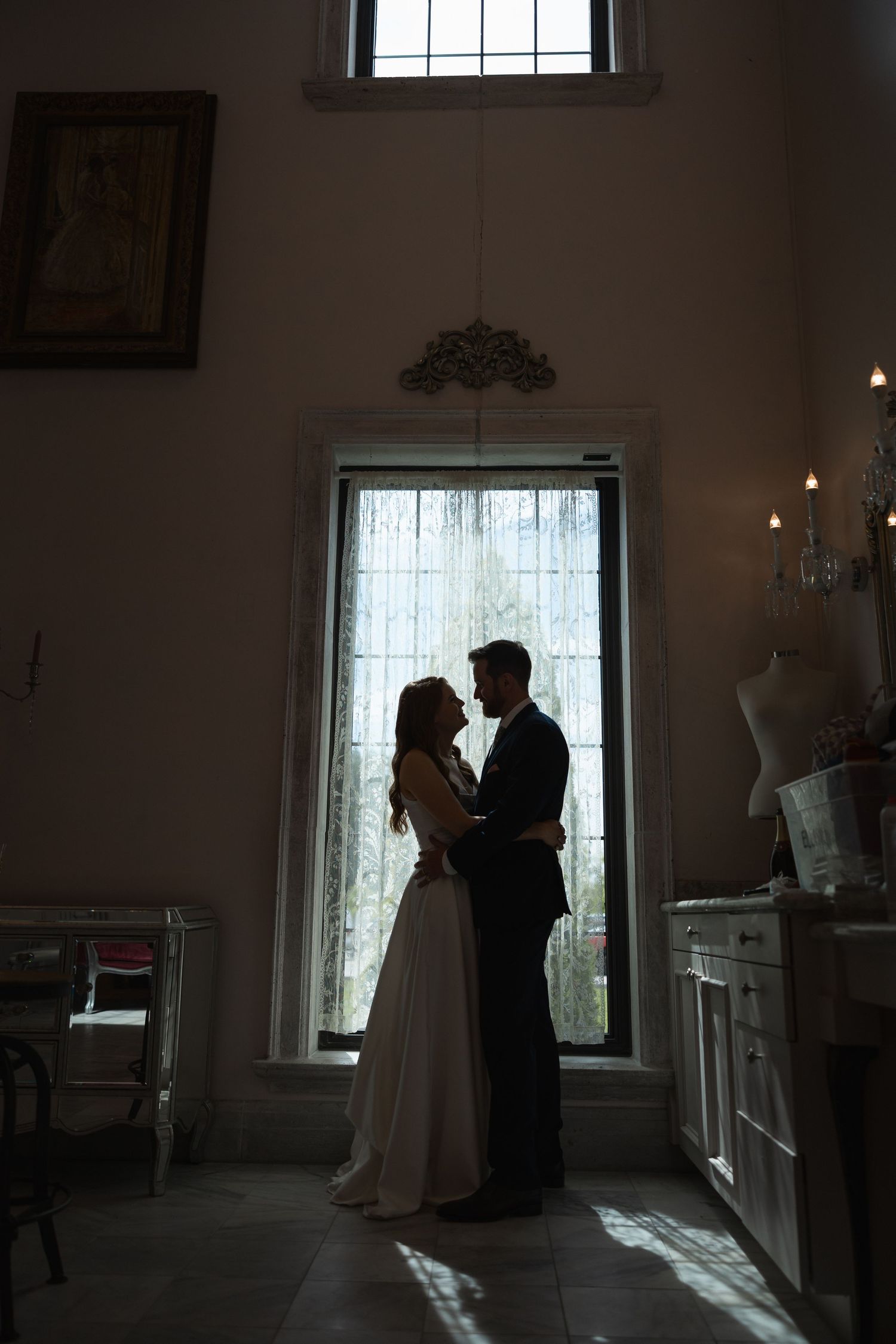 Elegant wedding scene with silhouettes against bright windows in a classic indoor setting.